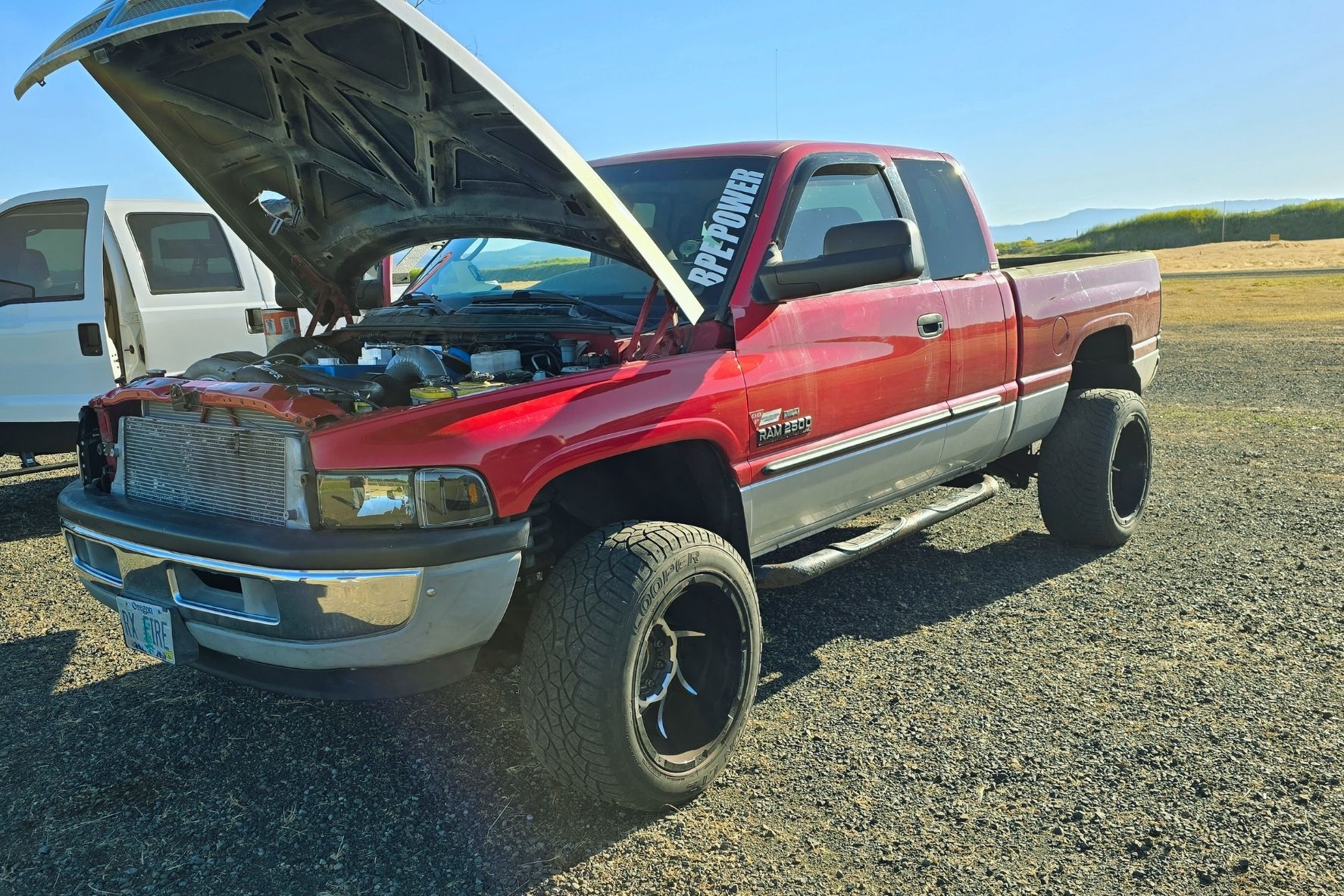 Red Dodge Ram 2500 truck with raised suspension, black wheels, and its hood open showing the engine.