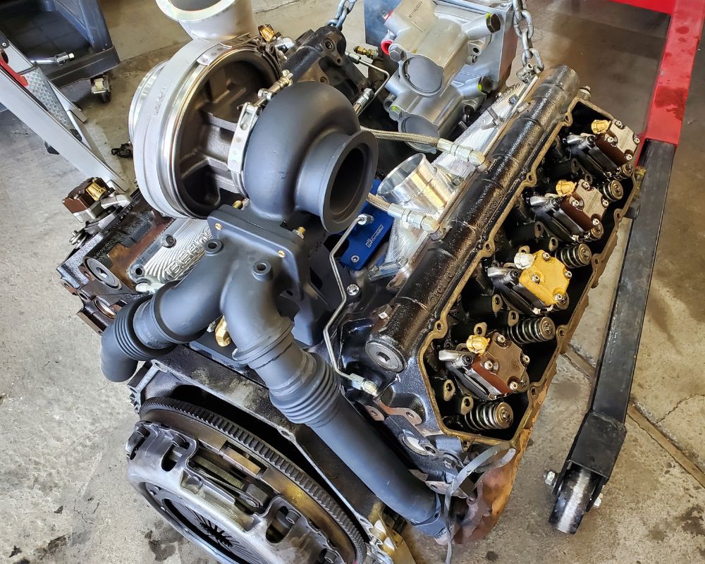 A high-performance V8 engine with a large turbocharger mounted on an engine hoist in a workshop.